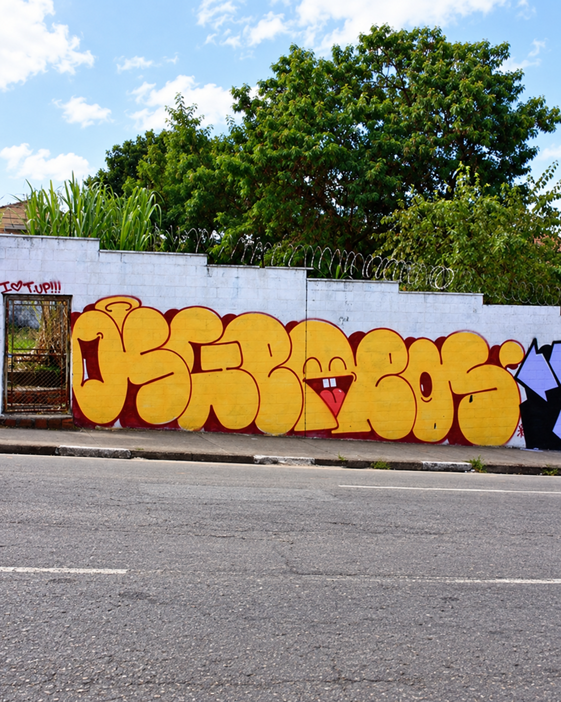 Yellow OSGEMEOS graffiti letters across a white street wall